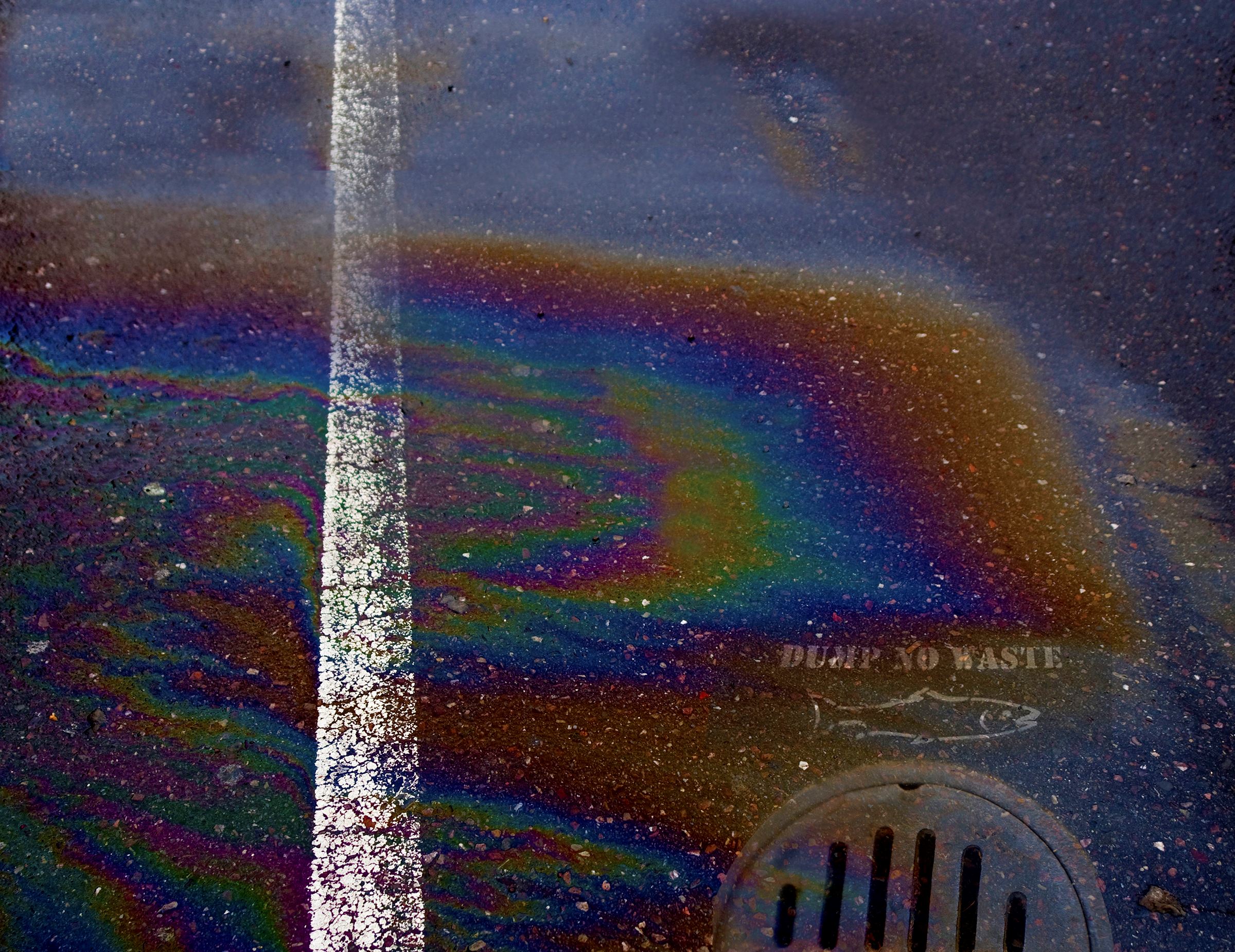 Close-up of a rainbow oil slick on street going into drain.