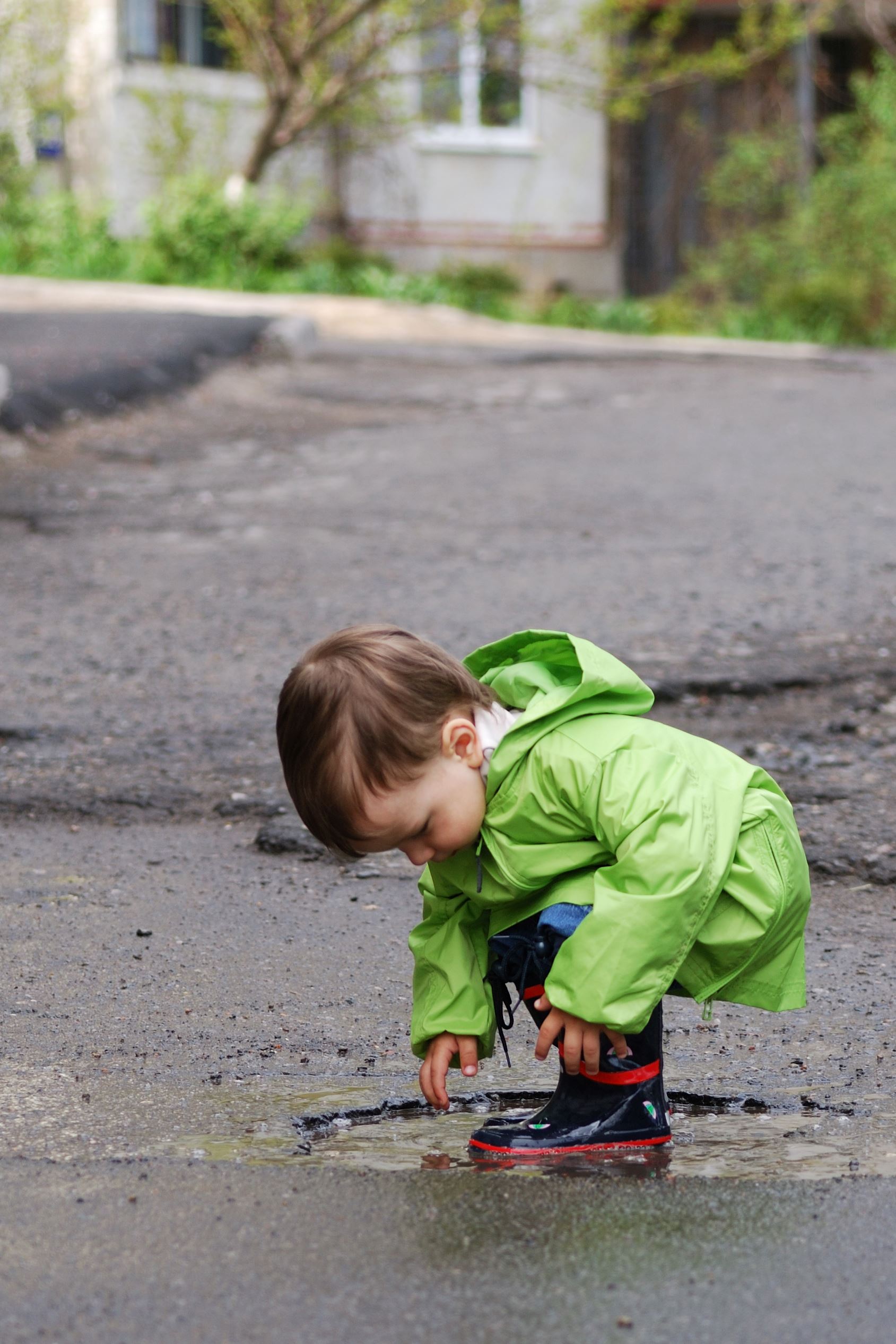 Boy in green coat bending down to touch puddle.